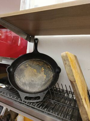 A rusty cast iron pan sitting on the drying rack above the sink